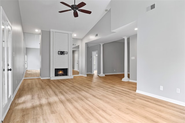 unfurnished living room with high vaulted ceiling, a brick fireplace, light wood-type flooring, ceiling fan, and decorative columns