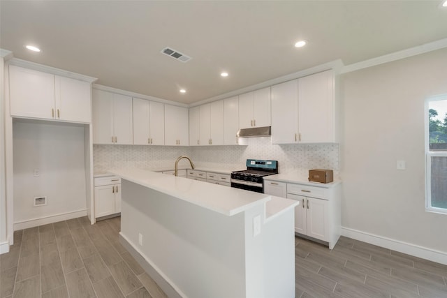 kitchen featuring a kitchen island with sink, backsplash, stainless steel gas range, and white cabinets