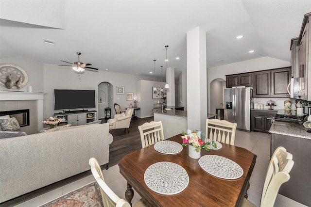 dining room with ceiling fan, light hardwood / wood-style floors, vaulted ceiling, and a tiled fireplace