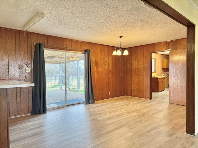 unfurnished dining area with a textured ceiling, a notable chandelier, light wood-type flooring, and wood walls