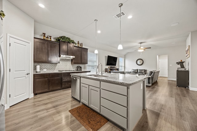 kitchen featuring a kitchen island with sink, sink, light stone counters, appliances with stainless steel finishes, and decorative backsplash