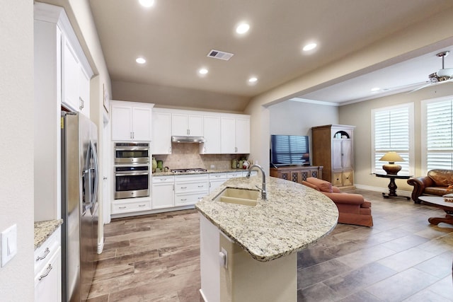 kitchen featuring open floor plan, stainless steel appliances, a sink, and white cabinets