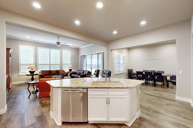 kitchen with light stone counters, a sink, white cabinetry, open floor plan, and stainless steel dishwasher