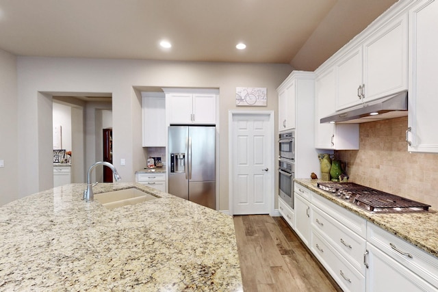 kitchen featuring light stone counters, under cabinet range hood, a sink, white cabinetry, and appliances with stainless steel finishes