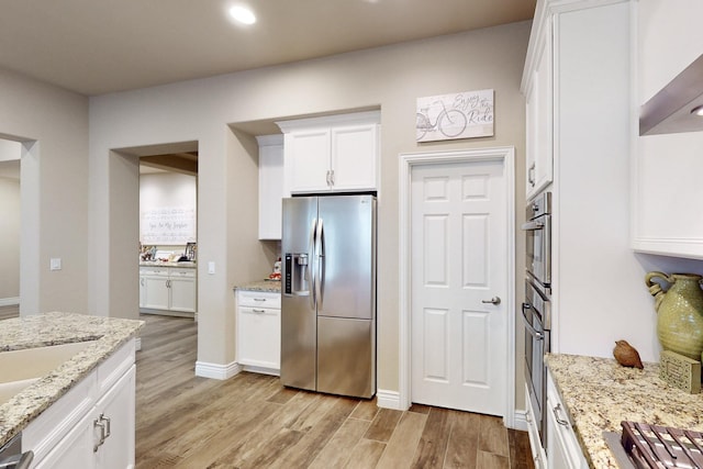 kitchen with light stone counters, appliances with stainless steel finishes, white cabinets, light wood-type flooring, and baseboards