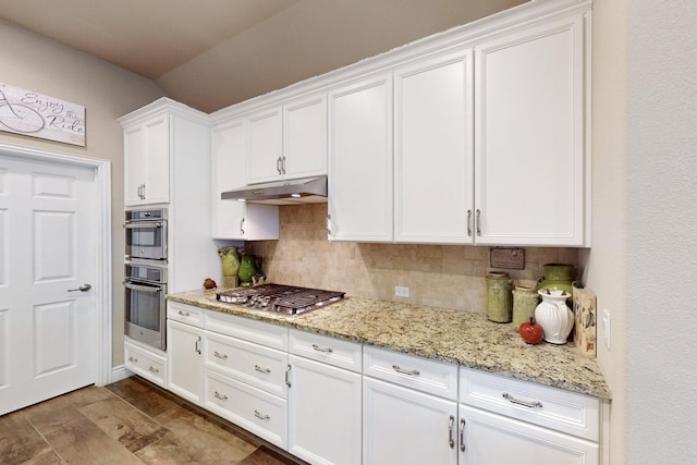 kitchen featuring under cabinet range hood, stainless steel appliances, white cabinets, light stone countertops, and tasteful backsplash