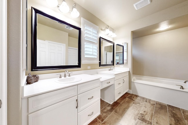 full bath featuring vanity, visible vents, a bath, and wood finish floors