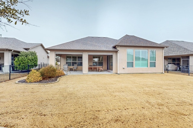 rear view of house featuring a lawn, roof with shingles, fence, a patio area, and stucco siding