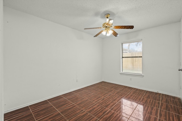 empty room with dark tile patterned flooring, ceiling fan, a textured ceiling, and baseboards