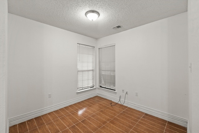 unfurnished room featuring a textured ceiling, dark wood-type flooring, visible vents, and baseboards