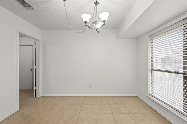 spare room featuring a notable chandelier, light tile patterned floors, visible vents, a textured ceiling, and baseboards