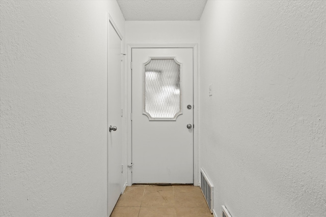 entryway with a textured ceiling, a textured wall, light tile patterned floors, and visible vents