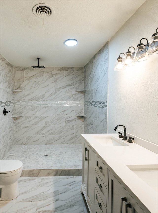 bathroom featuring vanity, a tile shower, and toilet