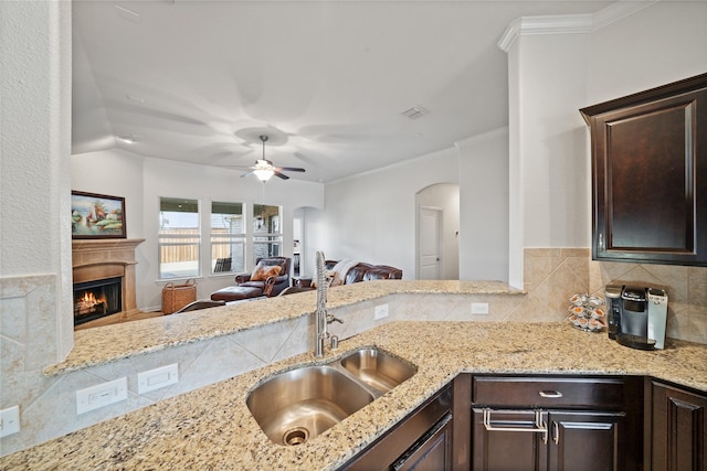 kitchen with light stone counters, sink, dark brown cabinets, and ornamental molding