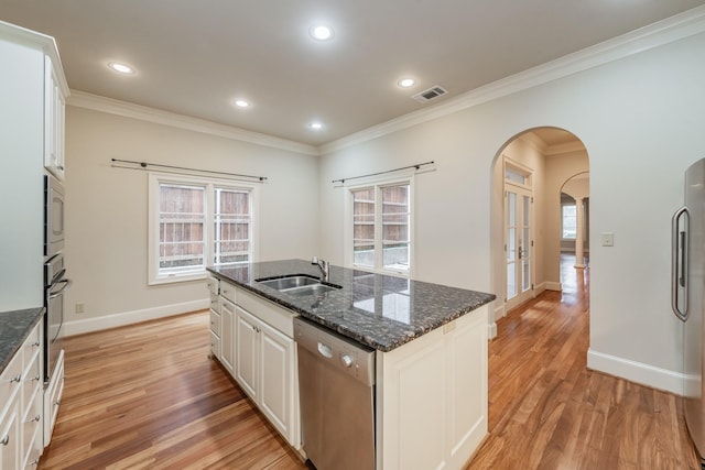 kitchen with sink, dark stone countertops, white cabinets, stainless steel appliances, and a center island with sink