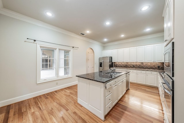 kitchen with white cabinetry, dark stone countertops, stainless steel appliances, a center island with sink, and decorative backsplash