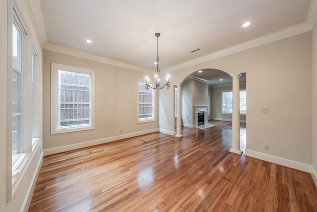 unfurnished dining area with a notable chandelier, hardwood / wood-style flooring, ornamental molding, and ornate columns