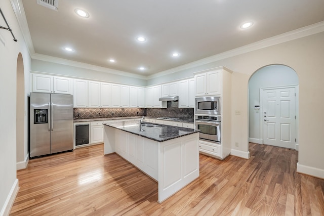 kitchen featuring appliances with stainless steel finishes, an island with sink, sink, white cabinets, and dark stone counters