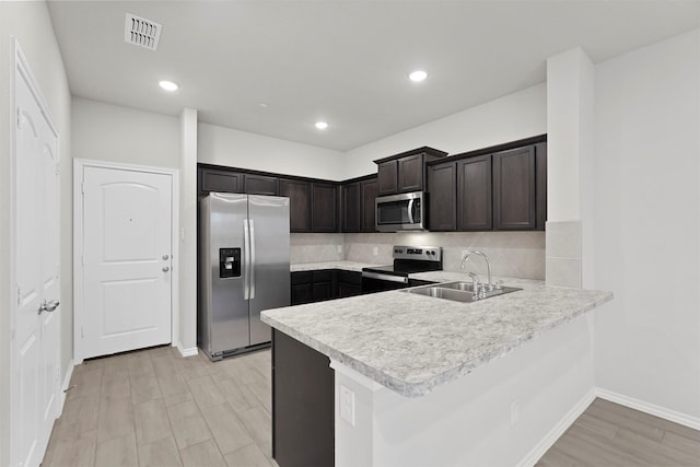 kitchen featuring sink, stainless steel appliances, tasteful backsplash, dark brown cabinetry, and kitchen peninsula