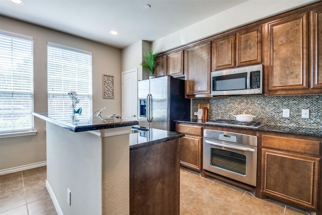 kitchen with stainless steel appliances, tasteful backsplash, a kitchen island with sink, and light tile patterned floors