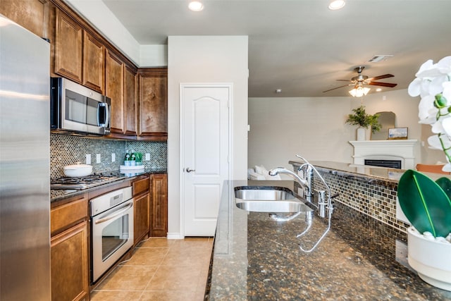 kitchen featuring sink, dark stone counters, light tile patterned floors, stainless steel appliances, and decorative backsplash