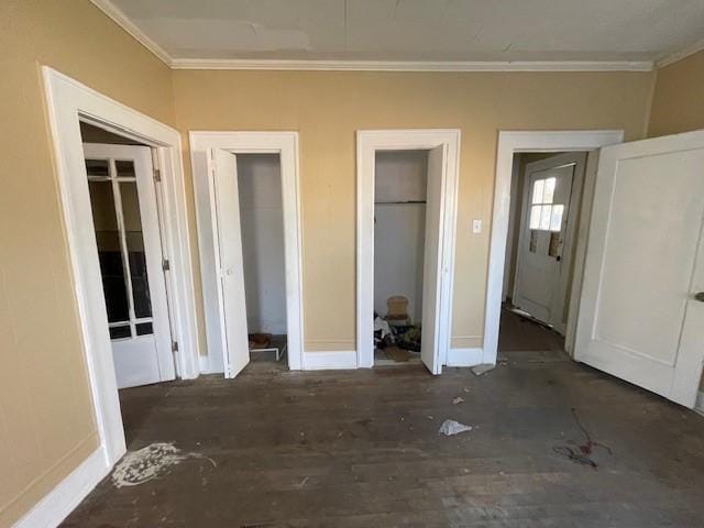 unfurnished bedroom featuring dark hardwood / wood-style flooring, ornamental molding, and multiple closets