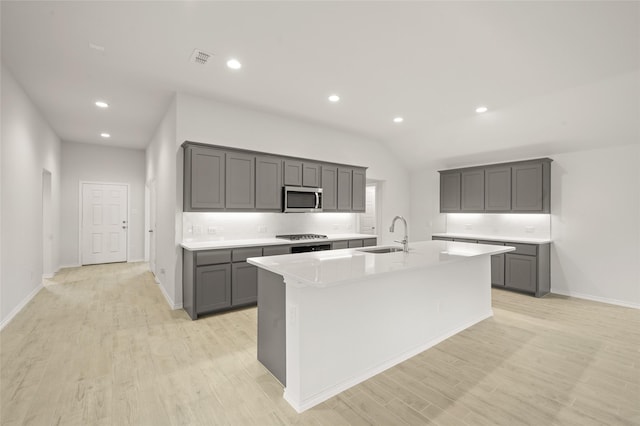 400 Basalt Dr, Azle, TX 76020 - kitchen with stainless steel microwave, a sink, an island with sink, decorative backsplash, and light wood-style flooring