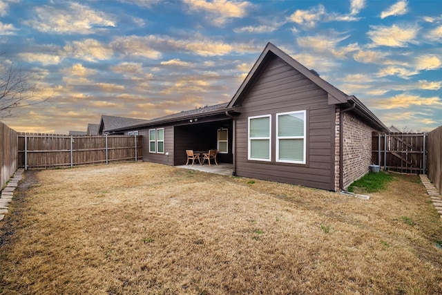 back house at dusk featuring a yard and a patio area