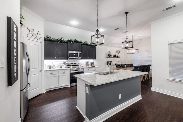 kitchen with sink, appliances with stainless steel finishes, hanging light fixtures, light stone counters, and an island with sink