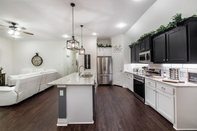 kitchen with dark wood-type flooring, sink, appliances with stainless steel finishes, pendant lighting, and a kitchen island with sink