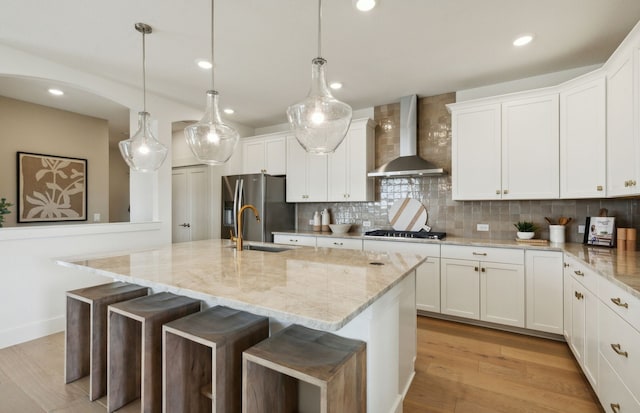 kitchen featuring wall chimney exhaust hood, sink, white cabinetry, an island with sink, and stainless steel appliances