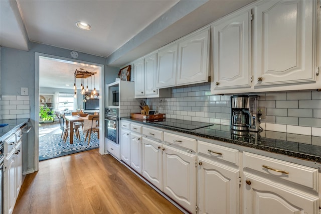 kitchen with dark stone counters, black appliances, light wood-type flooring, and white cabinets