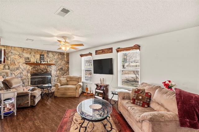 living room with dark hardwood / wood-style flooring, a stone fireplace, a textured ceiling, and ceiling fan