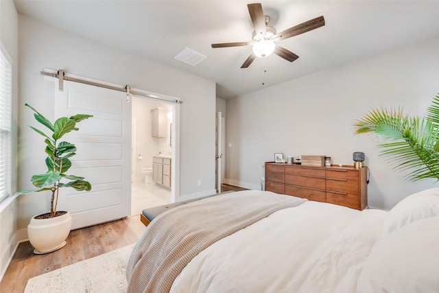 bedroom with ceiling fan, ensuite bath, a barn door, and light hardwood / wood-style flooring