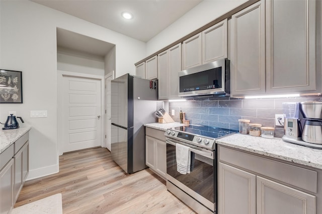 kitchen featuring light stone countertops, decorative backsplash, light hardwood / wood-style flooring, and stainless steel appliances