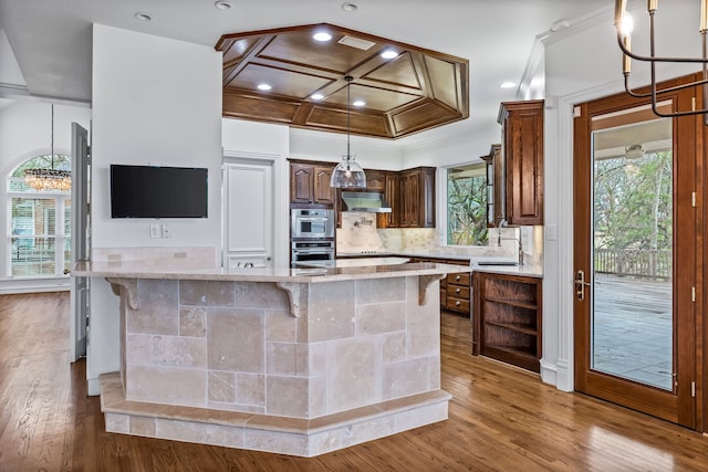 kitchen with tasteful backsplash, a kitchen bar, coffered ceiling, light stone counters, and light hardwood / wood-style flooring