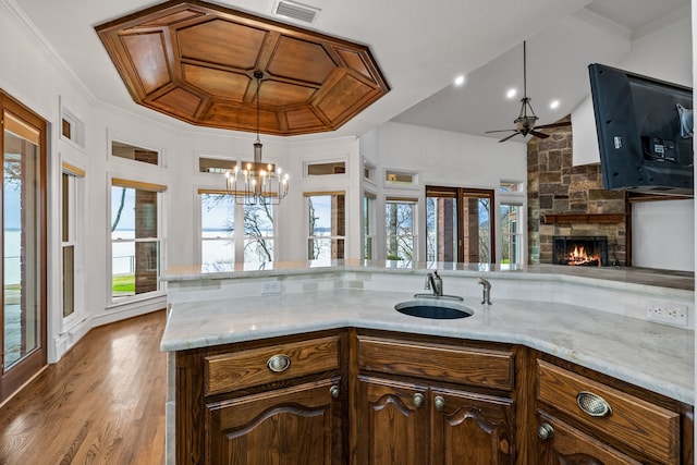 kitchen featuring a stone fireplace, sink, crown molding, dark brown cabinets, and light hardwood / wood-style flooring