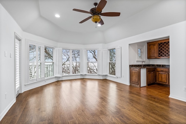 unfurnished living room with dark hardwood / wood-style flooring, ceiling fan, a tray ceiling, and indoor wet bar