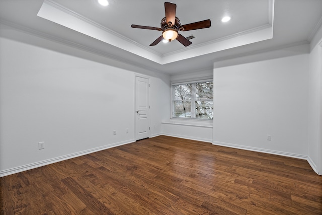 empty room featuring ornamental molding, dark wood-type flooring, ceiling fan, and a tray ceiling