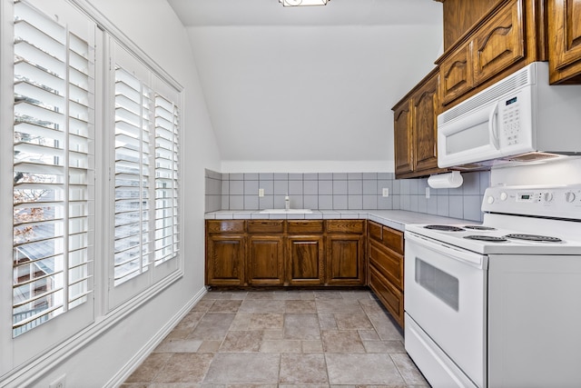 kitchen with white appliances, vaulted ceiling, and decorative backsplash