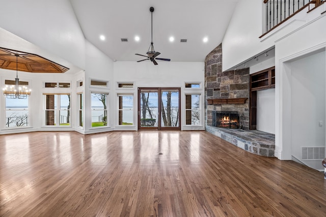 unfurnished living room featuring ceiling fan with notable chandelier, a fireplace, wood-type flooring, and a towering ceiling