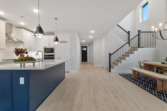 kitchen featuring pendant lighting, appliances with stainless steel finishes, wall chimney exhaust hood, and white cabinets