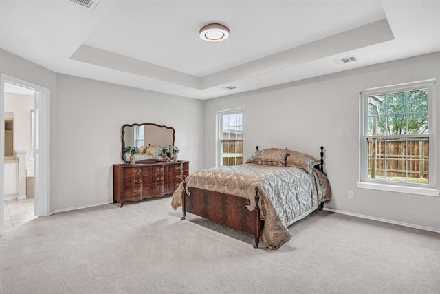 bedroom featuring a tray ceiling, light carpet, multiple windows, and ensuite bath