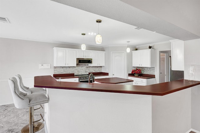 kitchen with appliances with stainless steel finishes, kitchen peninsula, white cabinets, hanging light fixtures, and tasteful backsplash