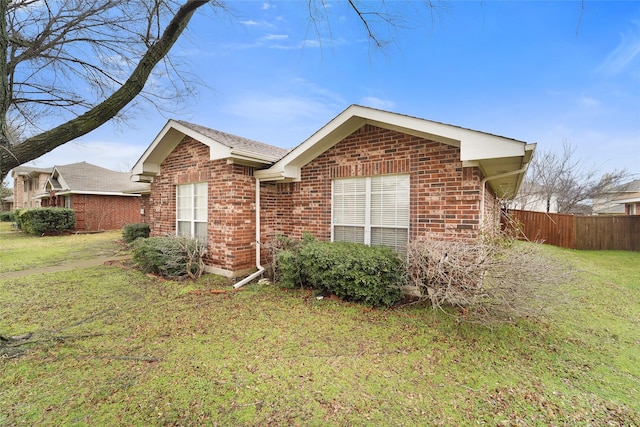 view of side of property featuring brick siding, a lawn, and fence