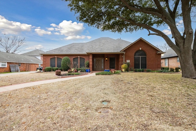 view of front of house featuring a front yard, brick siding, and a shingled roof