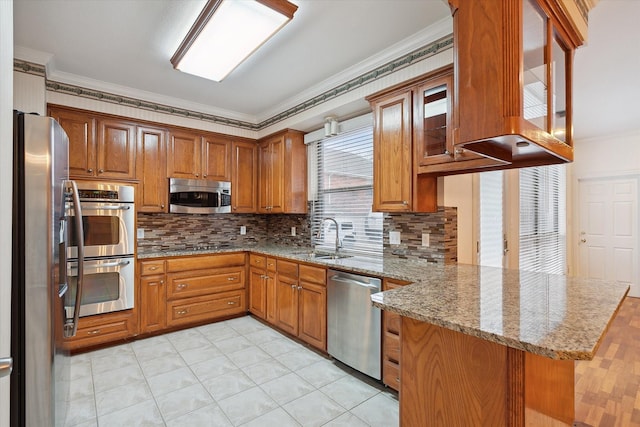 kitchen with brown cabinetry, a peninsula, a sink, appliances with stainless steel finishes, and crown molding