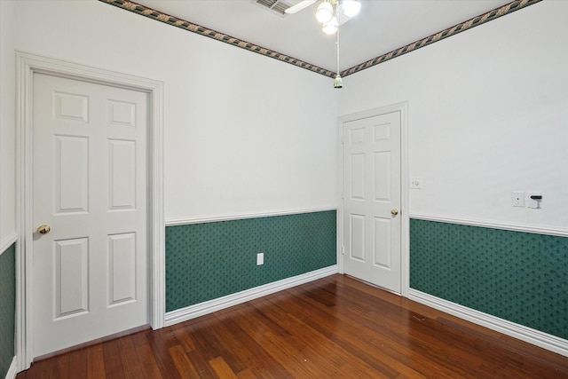 empty room featuring a wainscoted wall, a ceiling fan, hardwood / wood-style flooring, wallpapered walls, and baseboards