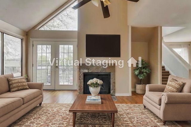 living room with hardwood / wood-style flooring, ceiling fan, high vaulted ceiling, a tiled fireplace, and french doors