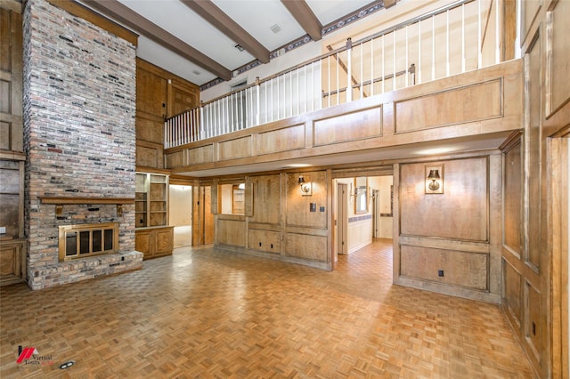 unfurnished living room featuring a fireplace, beamed ceiling, light parquet flooring, and wood walls